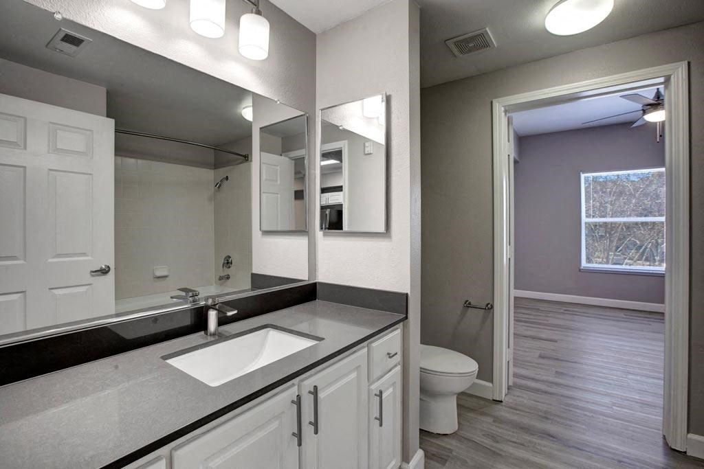 A bathroom with a sink, mirror, toilet and wooden floors.