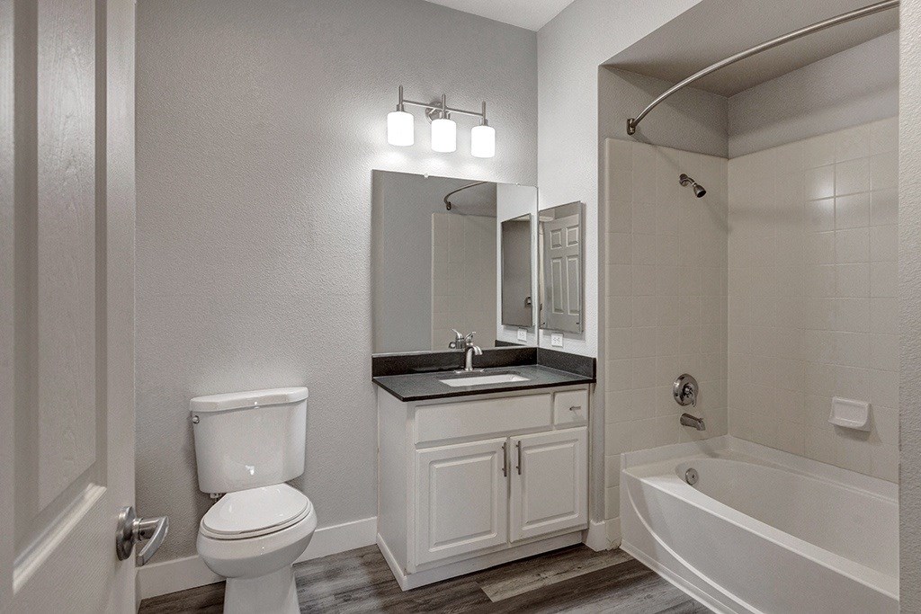 A white toilet is in a bathroom with a white tub.