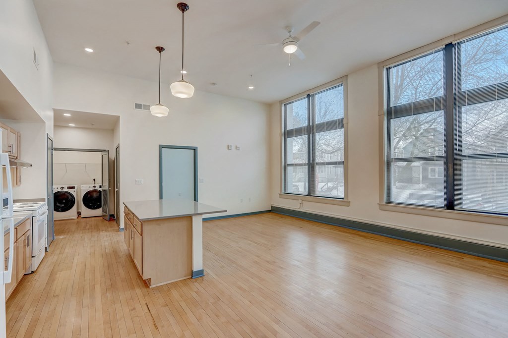 an empty living room with a kitchen and a large window