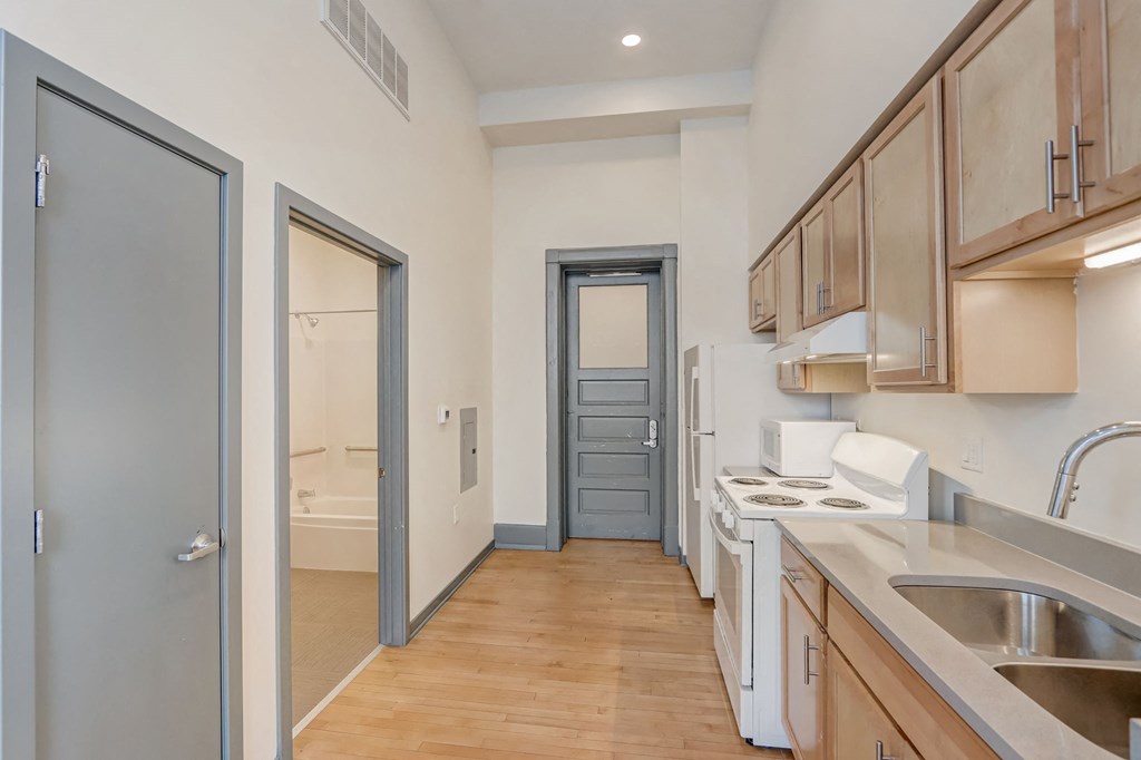 a kitchen with wood flooring and wooden cabinets and a door to a bathroom