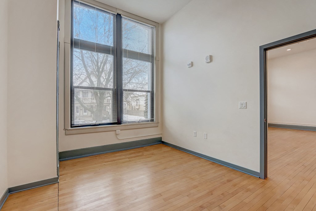 a bedroom with a large window and wood flooring and a mirrored door