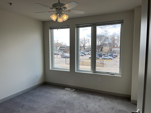A room with a ceiling fan and two windows overlooking a parking lot.