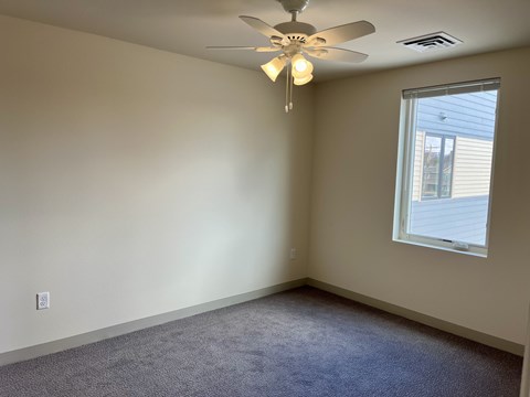 A room with a ceiling fan and carpeted floor.