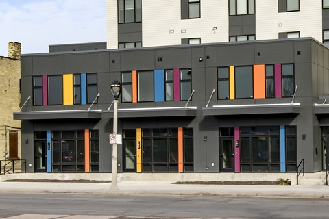 A building with a grey facade has a row of windows with brightly colored panels on them.