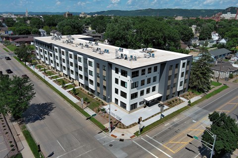 A large white building with a flat roof is surrounded by a road and trees.