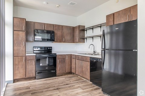 A black fridge sits in a kitchen with wooden cabinets and a black oven.