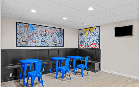 A room with blue chairs and tables and two paintings on the wall.