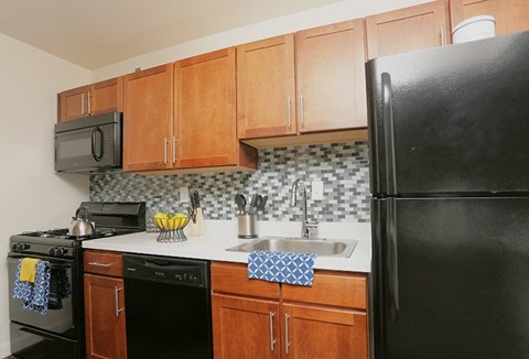 A black refrigerator stands in a kitchen with wooden cabinets and a black microwave.