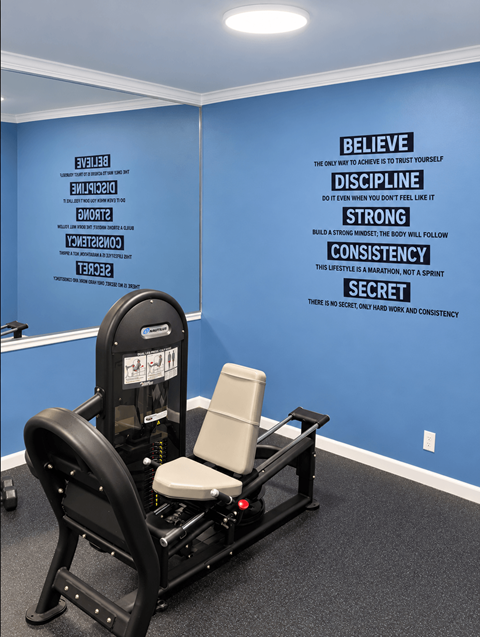 A gym room with a row of exercise machines and a wall with inspirational words.
