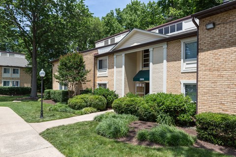 A building with a green awning is surrounded by bushes and trees at Potomac Ridge Apartments, Woodbridge, Virginia