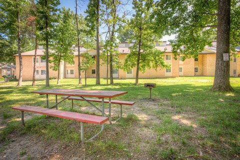 A picnic table is in the foreground of a grassy area with trees and a building in the background at Potomac Ridge Apartments, Virginia