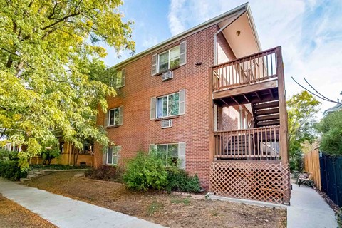 A red brick apartment building with a balcony and a tree in front.