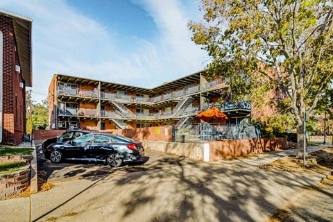 A black car is parked in front of a multi-story apartment building.