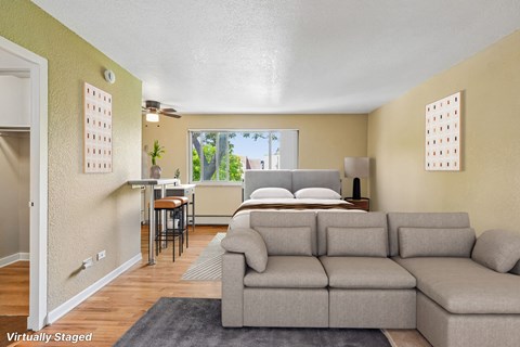 A living room with a grey couch and a bed in the background.