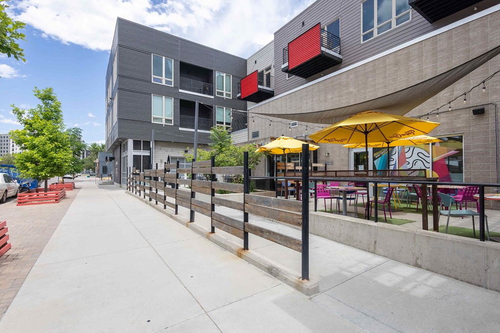 a sidewalk in front of a building with tables and umbrellas