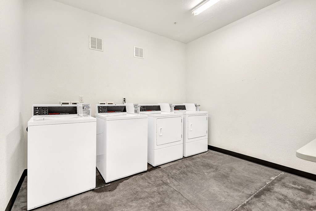 four washing machines and dryers in a row in a room with a cement floor