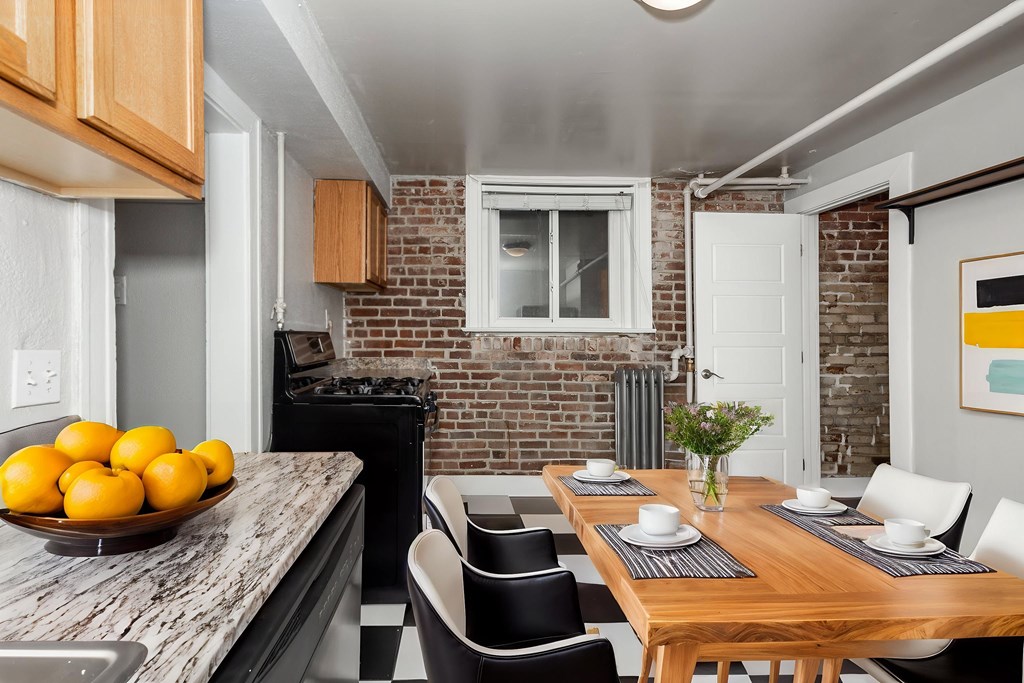 A kitchen with a table set for two with a bowl of oranges on the counter.