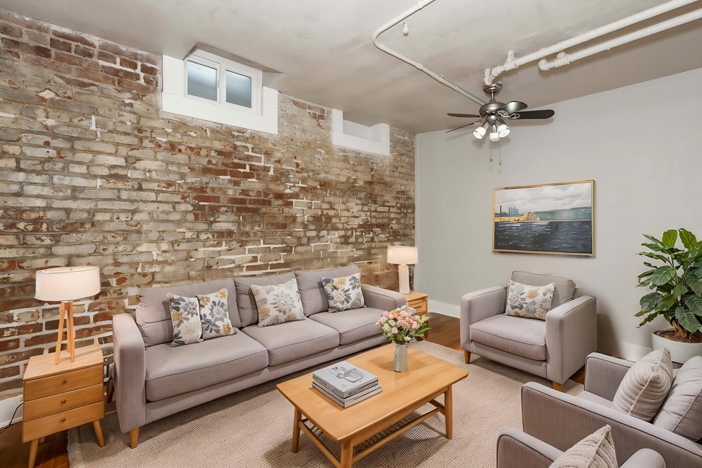 A living room with a grey couch, a coffee table, a chair, a potted plant, and a painting on the wall.