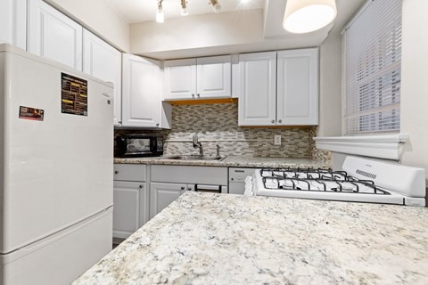 an updated kitchen with white cabinets and granite counter tops and a white refrigerator and stove