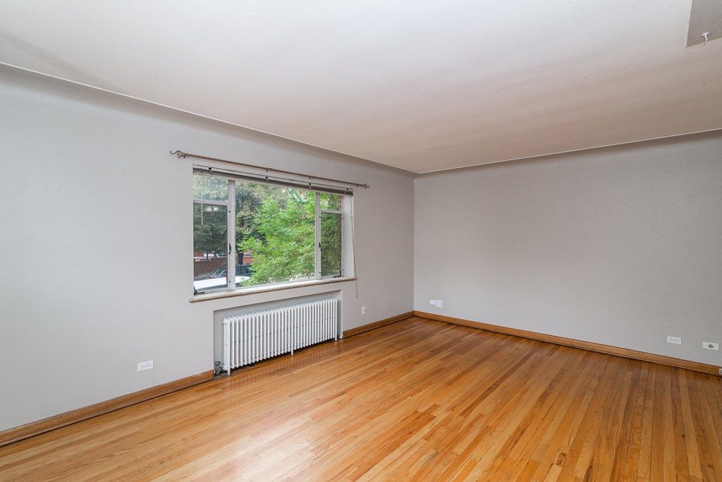 A room with wooden floors and a window with a white radiator beneath it.