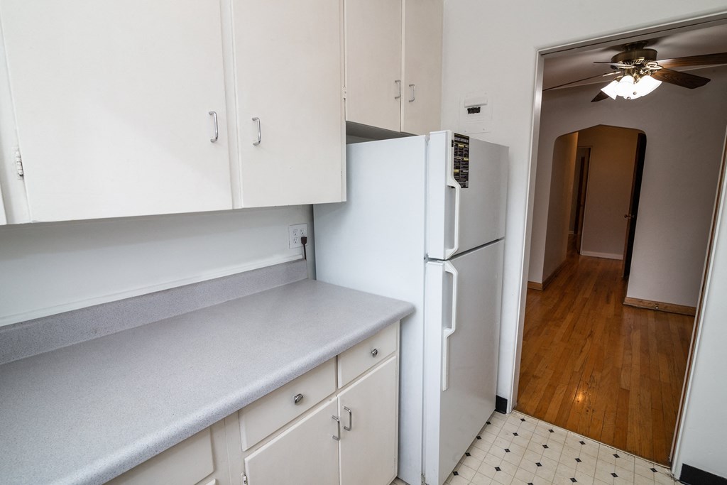 A white refrigerator is in a kitchen with white cabinets.