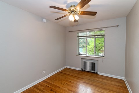 A room with a ceiling fan and a window with a view of trees.