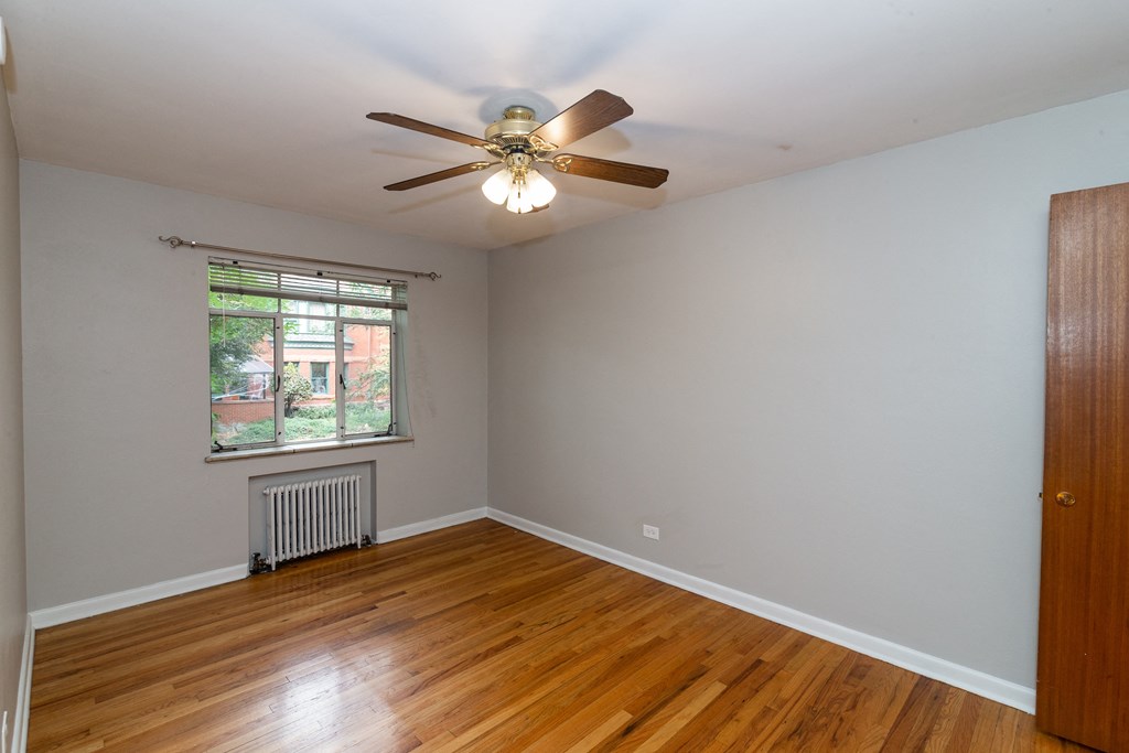 A room with a ceiling fan and a window with a view of a tree.