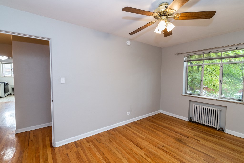 A room with a ceiling fan and a window with a view of trees.