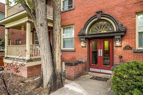 A red brick house with a red door and a window with a red curtain.