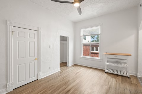 A room with a white door, a window with a view of a brick building, and a wooden bench.