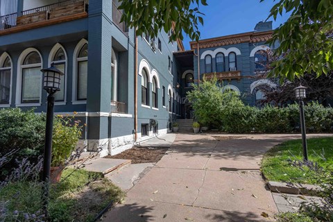 a sidewalk in front of two blue buildings with trees and bushes
