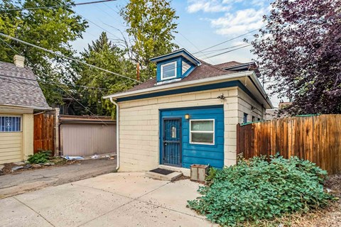 A small house with a blue door is surrounded by a wooden fence.
