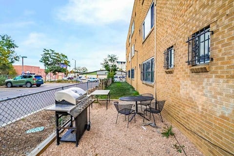 A patio with a grill and chairs is in front of a brick building.