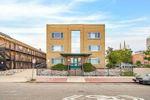 A brick building with a green awning sits in front of a black fence.