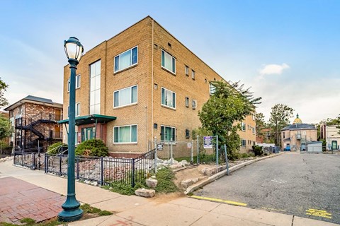 A street view of a residential area with a brick building, a lamp post, and a fence.