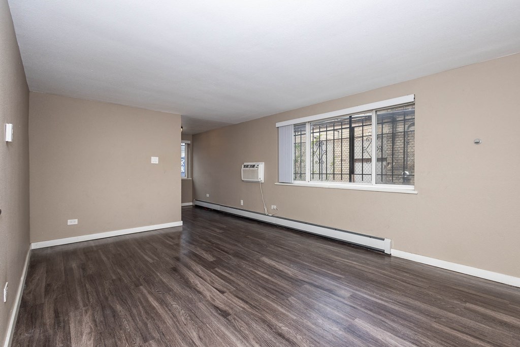 A room with wooden flooring and a window with bars on it.