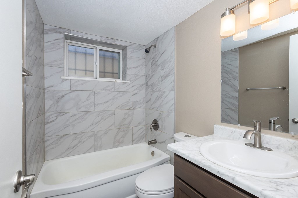 A white bathtub sits next to a toilet in a bathroom with marble tiles.