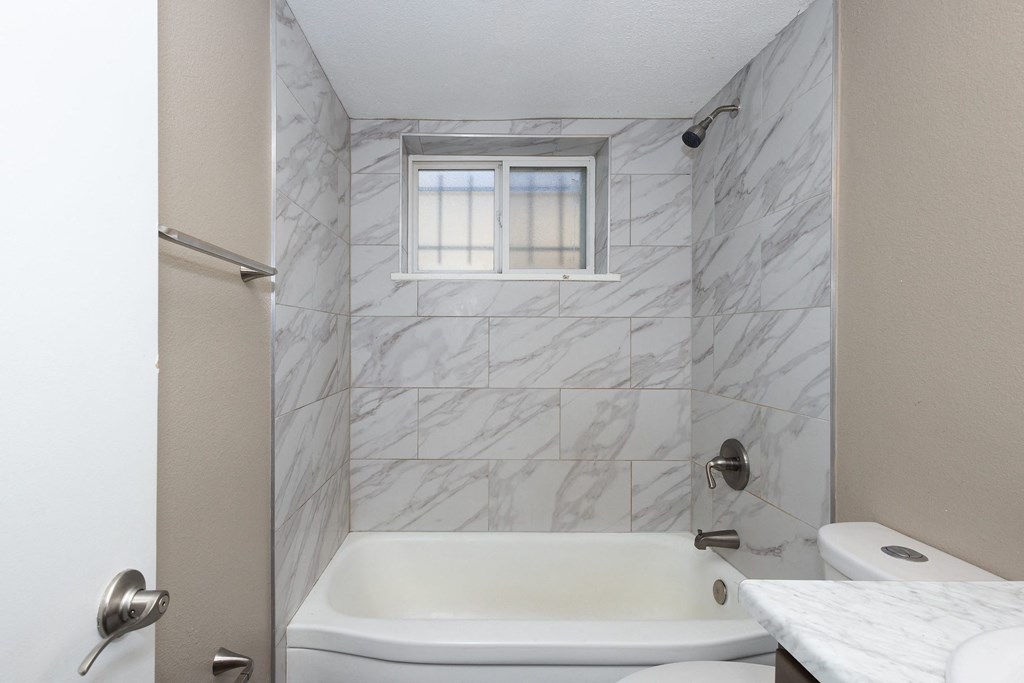 A white bathroom with a marble tile wall and a window.