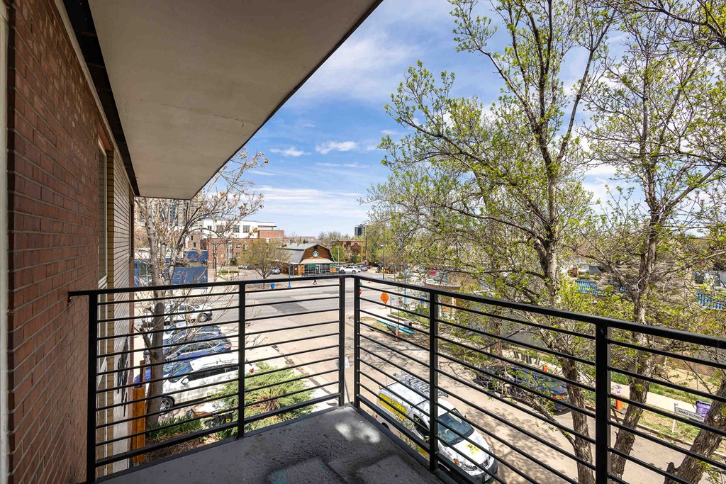 A balcony with a black railing overlooks a parking lot and trees.