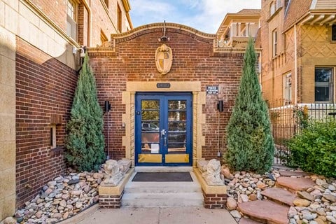 A blue door is flanked by two trees and a stone wall.