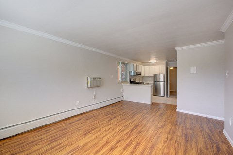 an empty living room with wood flooring and a kitchen