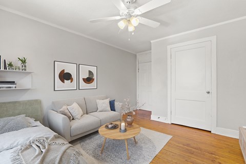 A living room with a grey couch, a wooden table, and a ceiling fan.