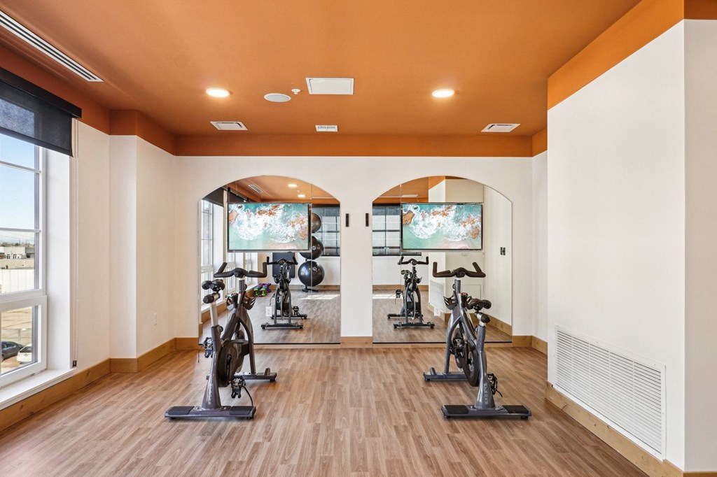 A spacious room with a row of exercise bikes and a television.