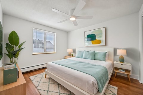 A bedroom with a bed, a ceiling fan, and a painting on the wall.