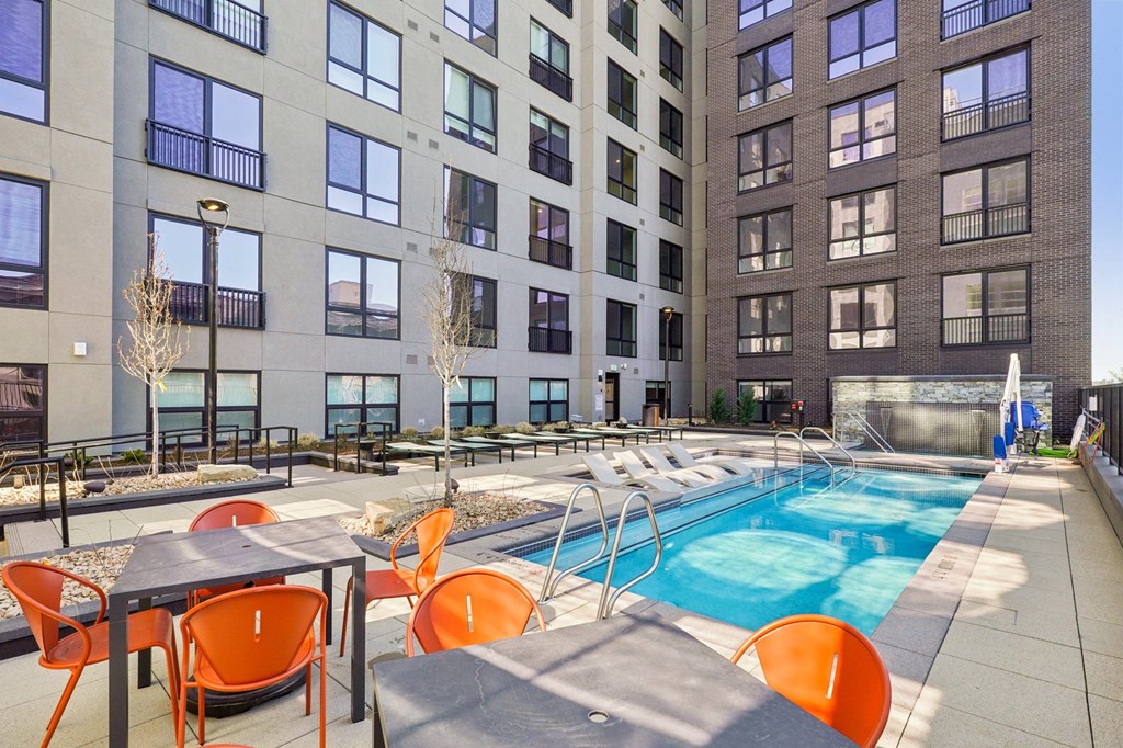 A pool surrounded by orange chairs and tables in front of a building.