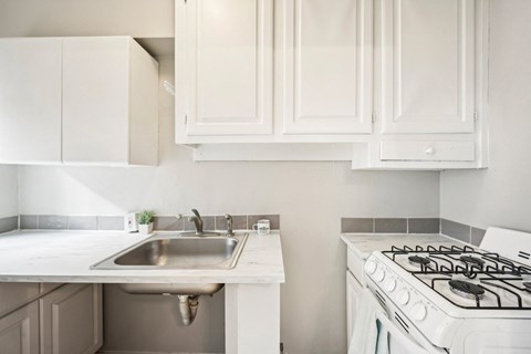 a white kitchen with a sink and stove and white cabinets
