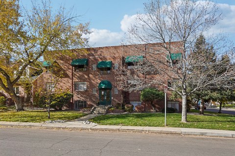 A red brick building with green awnings sits on a street corner.