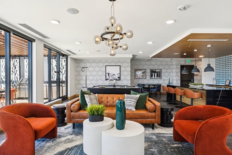 A modern living room with a brown sofa, orange chairs, and a chandelier.
