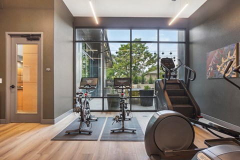A gym with exercise equipment and a view of trees outside the window.