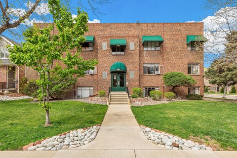 A red brick building with green awnings and a stone pathway leading to the front door.